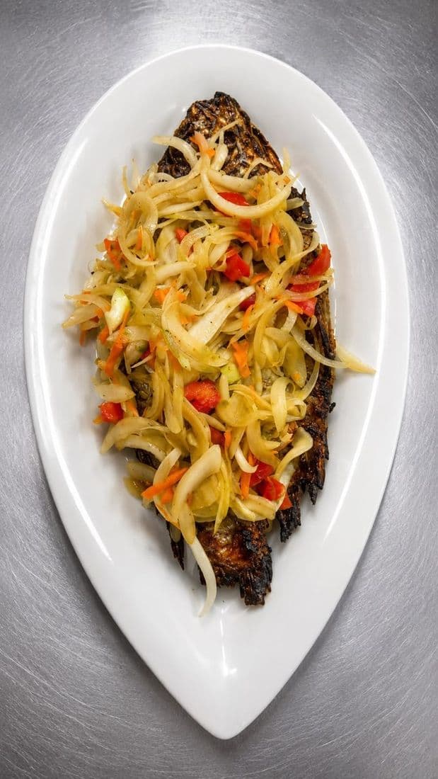 Poisson braisé entier garni d'oignons et de piments, servi dans une assiette ovale blanche